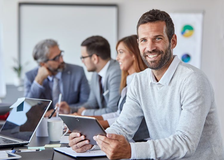 Man smiling at camera holding a laptop in conference room happy because he has achieved the 5 Digital Transformation Success Factors